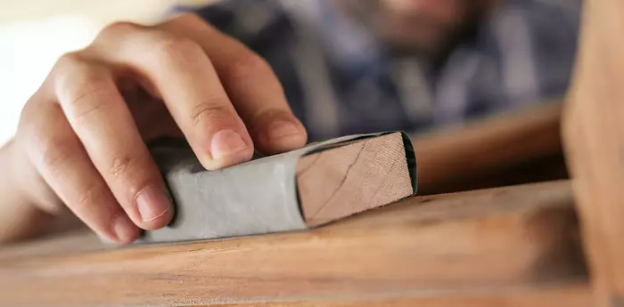 A man grinds wood with sandpaper
