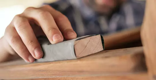 A man grinds wood with sandpaper